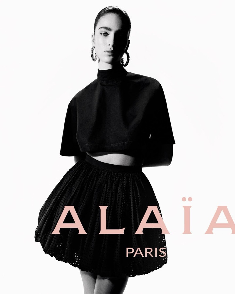 Loli Bahia presents Alaïa's summer-fall 2024 collection, donning a chic black outfit with a crop top and skirt.