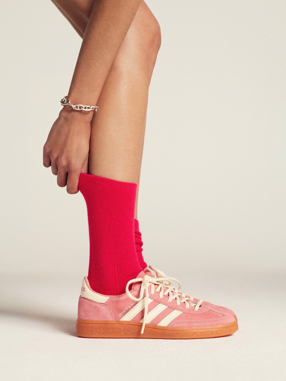 The new pastel pink Handball Spezial sneakers from adidas Originals x Sporty & Rich, styled with red socks.