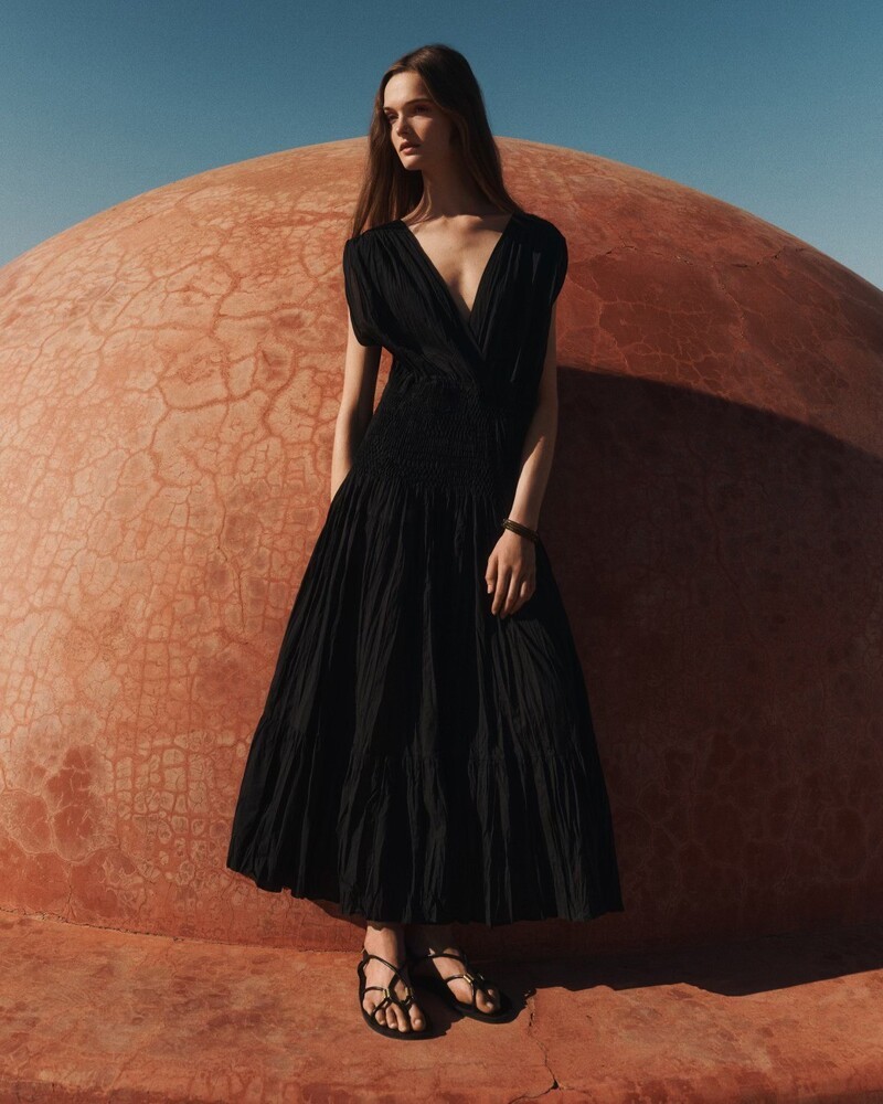 Lulu Tenney stands against a terracotta dome in a black maxi dress dress for Massimo Dutti summer 2024.