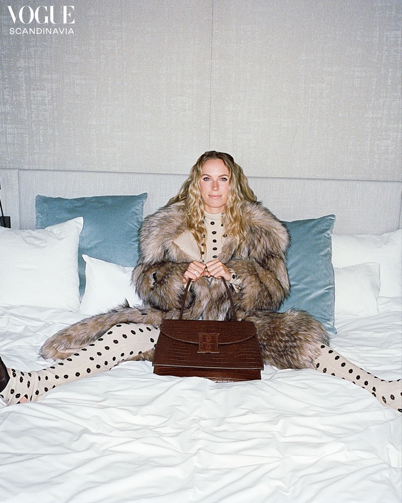 Tennis player Caroline Wozniacki poses in bed wearing a fluffy coat.