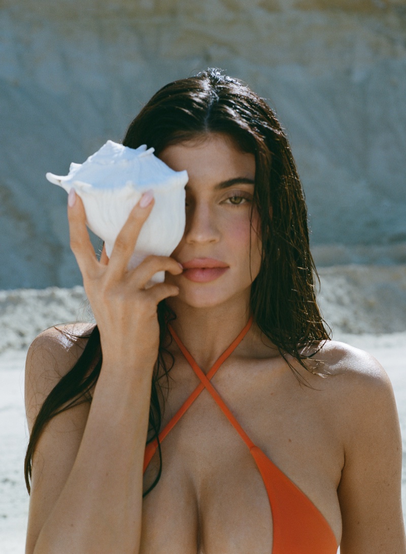 Kylie Jenner poses with a seashell in an orange bikini top.