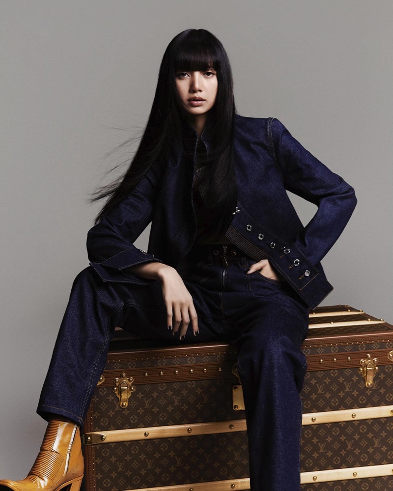 Lisa models a jean jacket and pants while posing on a Louis Vuitton trunk.