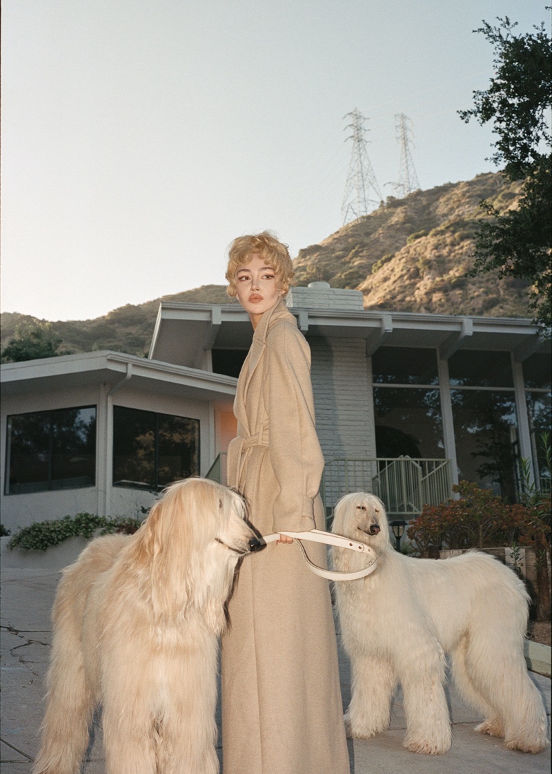 Nadia Lee Cohen poses with Afghan hounds in a tan overcoat for & Other Stories' fall 2024 campaign.