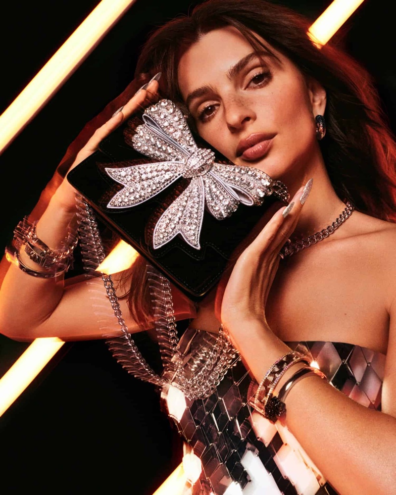 Emily Ratajkowski models Kurt Geiger's Shoreditch Bow bag in from its Holiday 2024 collection.