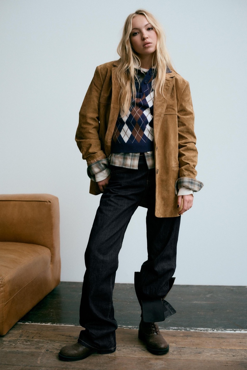 Layering up, Lila Moss poses in tan jacket, argyle print sweater, and baggy jeans from Zara.